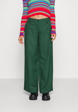 Pantalones anchos verdes hechos de una tela texturizada, con cierre de botón en el frente y bolsillos laterales, combinados con un suéter de rayas colorido.
