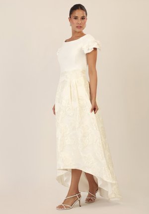 Weißes Kleid mit taillierter Oberseite, Puffärmeln und einem schwingenden Rock mit einem strukturierten Blumenmuster. Ergänzt durch weiße Riemchen-Heels.