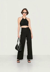 Top halter cropped preto apresenta detalhes intrincados; combinado com calças largas pretas de cintura alta. Acessórios incluem uma pequena bolsa preta e óculos de sol.
