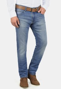 Jeans de mezclilla azul claro con un corte ajustado, textura desgastada y un cinturón de cuero marrón. Combinados con botas de ante marrón hasta el tobillo.