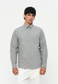 Camicia a righe nei toni del blu e del giallo. Presenta maniche lunghe, un colletto e una tasca sul petto con una vestibilità comoda.