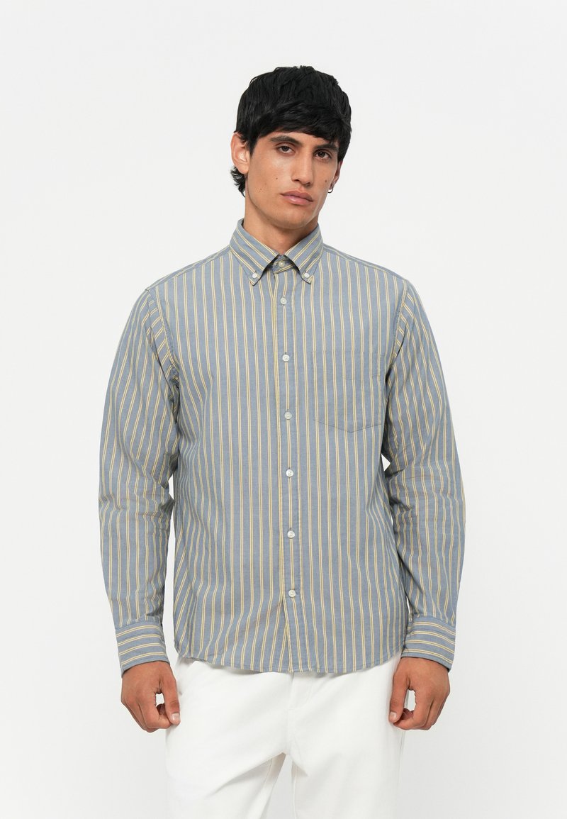 Camicia a righe nei toni del blu e del giallo. Presenta maniche lunghe, un colletto e una tasca sul petto con una vestibilità comoda.