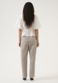 Vit linnetopp med peplum, korta puffärmar och samlad midja, kombinerad med ljusgrå tapered byxor och svarta högklackade skor.