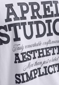 Lettres noires en gras épelant "APREI STUDIO," "AESTHET," et "SIMPLICI" avec des phrases en cursive "Artisan vraiment remarquable" et "Plus qu'une simple étiquette" sur un tissu blanc.