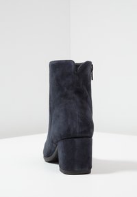 Marineblaue Wildleder-Stiefeletten mit runder Zehenpartie und Blockabsatz. Verfügt über einen Seitenreißverschluss und einen leicht geschwungenen Schaft. Glatte Textur und schlichtes Design.