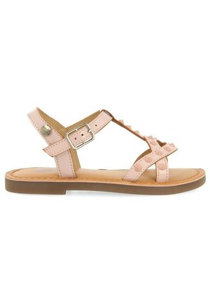 Sandalia de cuero rosa con un diseño de tiras, acentos de tachuelas, hebilla ajustable y suela plana marrón con plantilla acolchada.