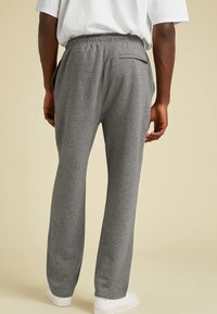 Hombre que lleva pantalones de chándal grises con cintura elástica y bolsillo trasero con cremallera, combinados con zapatillas blancas y una camiseta blanca.