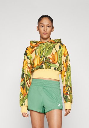Felpa corta con base gialla decorata da un motivo floreale verde e arancione; abbinata a pantaloni sportivi verdi con elastico in vita e logo.