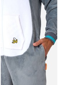 Un onesie gris y blanco hecho de material suave y de felpa. Presenta un plátano bordado en el bolsillo y una banda de color en las muñecas.
