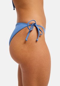 Bas de bikini bleu avec des liens sur les côtés, une texture lisse et une coupe taille basse, mis en valeur sur un fond clair.