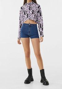 Graphic cropped top with "ERROR" text in purple on black, paired with high-waisted denim shorts. Model wears black zip-up boots.