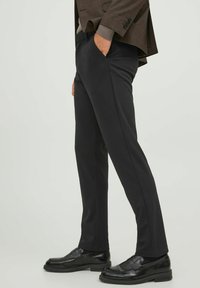 Black tailored trousers with a smooth texture, straight fit, side pockets, and subtle crease detailing. Paired with black loafers.