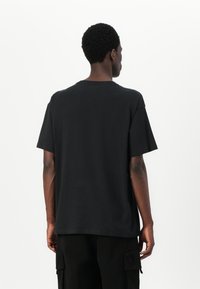 Black cotton t-shirt with short sleeves, round neckline, and relaxed fit. Smooth texture and minimal design, no visible logos or patterns.