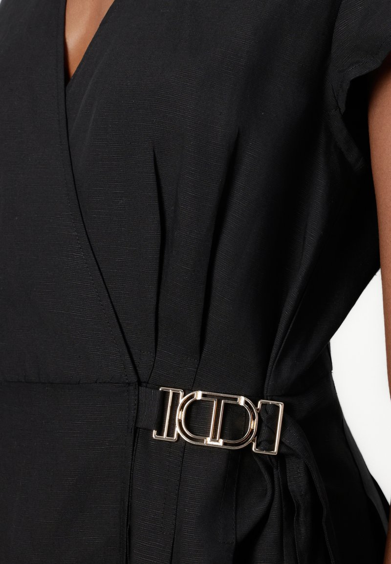 Czarna sukienka kopertowa z teksturowanej tkaniny i krótkimi rękawami, z złotą klamrą w pasie do zabezpieczenia talii.