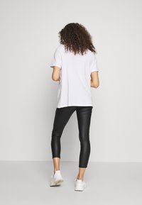 Vit t-shirt med kort ärm i kombination med svarta leggings i konstläder och vita sneakers. Outfiten har en avslappnad passform och en slät textur.