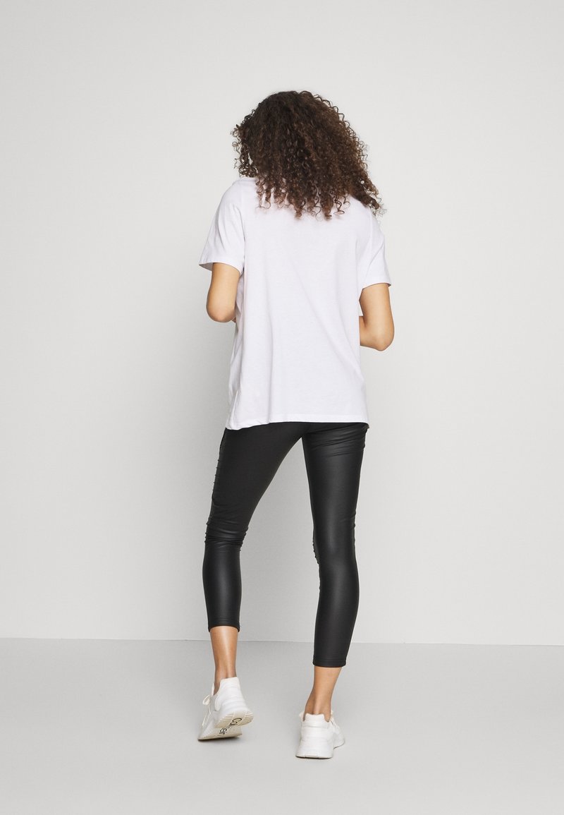 Vit t-shirt med kort ärm i kombination med svarta leggings i konstläder och vita sneakers. Outfiten har en avslappnad passform och en slät textur.