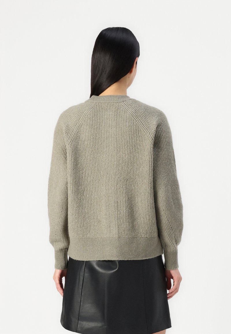 HellgrauerStrickpullover mit gerippter Textur, Rundhalsausschnitt und Raglanärmeln. Kombiniert mit einem schwarzen Lederrock, der eine bequeme Passform zeigt.