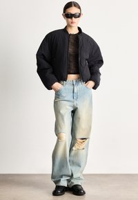 Čierna skrátená bomber bunda so zipsom, čierne grafické crop tričko, svetlomodré široké rifle s opotrebovaným vzhľadom a čierne masívne topánky.