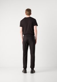 Svart kortermet t-skjorte og tapered bukser med elastisk midjebånd. Glatt tekstur med minimal detaljering, kombinert med svarte sko.