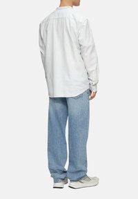 Gestreepte langsgemouwen shirt in lichtblauw en wit, gecombineerd met losse lichtblauwe jeans en neutrale sneakers, gezien van achteren.