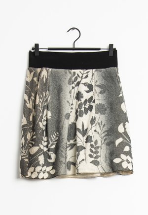 Černobílá sukně s květinovým vzorem a černým páskem visí na černém ramínku na bílém pozadí.