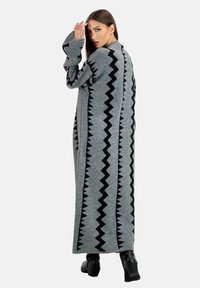 Lange grijze cardigan met een zwart zigzagpatroon aan de zijkanten. Gemaakt van zacht gebreid materiaal. Heeft brede mouwen en een losse pasvorm.