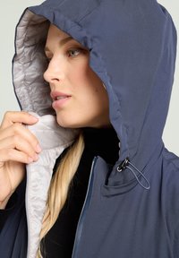Marineblaue Kapuzenjacke mit glatter Textur und leichter Innenfütterung. Ausgestattet mit verstellbarem Kordelzug, Reißverschluss und sichtbaren Nahtdetails.