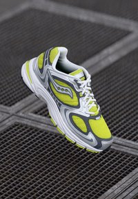 Sport sneaker with a gray mesh upper, bright yellow accents, white sole, and structured design. Features lace-up closure and textured panels.