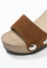 Braune Wildleder-Sandale mit einem breiten Riemen, Holzplattform, silbernen Akzenten und schwarzer Gummisohle. Verfügt über eine abgerundete Zehenpartie und eine glatte Textur.