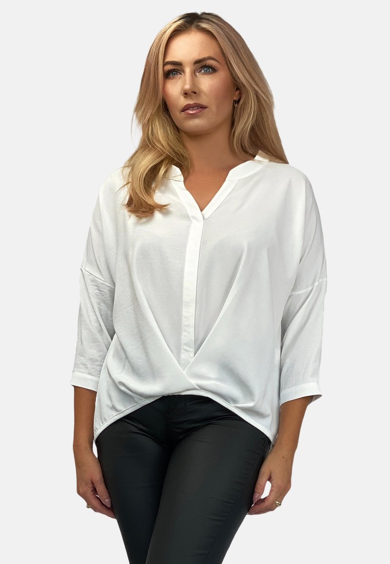 Weiße, lockere Bluse mit V-Ausschnitt, dreiviertellangen Ärmeln und einem verdrehten Frontdesign. Der Stoff wirkt glatt und leicht.