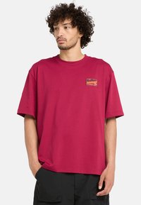 Camiseta de algodón burdeos con un corte relajado, con mangas cortas y un parche de logo cuadrado en el lado izquierdo del pecho.