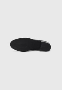 Chaussure en cuir noir avec une semelle en caoutchouc noir texturé, dotée d'un bout arrondi et d'un minimum de détails. Fini lisse et design épuré.