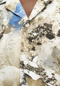 Κοντινό ενός πουκάμισου με κουμπιά με πολύχρωμο αφηρημένο σχέδιο από πέτρες και ορυκτά σε μπλε, μπεζ, μαύρους και λευκούς τόνους.