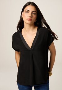 Blusa nera a maniche corte con scollatura a V profonda e rifiniture in raso, realizzata in tessuto leggero. Presenta una vestibilità ampia e una piegatura sottile.