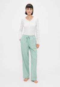 Top bianco a maniche lunghe con dettagli di bottoni abbinato a pantaloni da pigiama a righe verde chiaro con vita elasticizzata e lacci.
