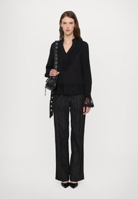 Bluză neagră cu mâneci lungi, cu dantelă pe margini, asociată cu pantaloni negri cu dungi și tocuri negre elegante. Accesorii cu o geantă mică neagră de umăr.