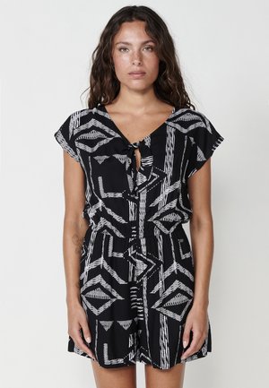 Robe noire avec des motifs abstraits blancs, détail en forme de trou de serrure au niveau du col, manches courtes, taille cintrée et coupe décontractée. Texture du tissu lisse.