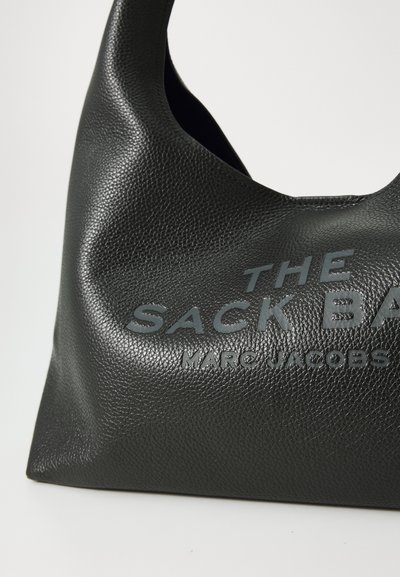 Must musträkk with tekstuuriga must nahkne kott. Omab laia, ümarat käepidet ja embosseeritud teksti "THE SACK BAG MARC JACOBS."
