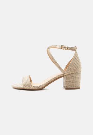 Sandale beige à talon bloc texturé, à bout ouvert, avec bride cheville et boucle dorée, vue de profil sur fond blanc.