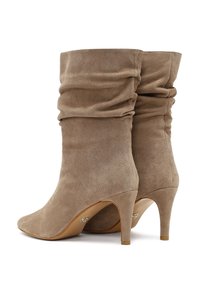 Botte alla caviglia in suede beige con un design sdrucito, punta appuntita e tacchi di 7,5 cm. Texture liscia e dettagli minimalisti sulla suola.