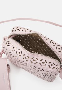 Jasnoróżowa torebka na ramię z kwiatowym wzorem wyciętym i srebrnym zamkiem, przedstawiona otwarta, obok niej dopasowany różowy portfel na białym tle.