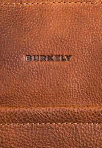 Billetera de cuero marrón con superficie texturizada, logo "BURKELY" en relieve y costuras en contraste para un detalle adicional.
