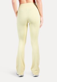 Hellgelbe, ausgestellte Leggings mit hohem Bund. Glattes, dehnbares Material mit minimalen Nahtdetails, von hinten gezeigt.