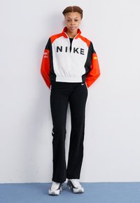 Nike zateplená bunda s červenobielo-čiernym farebným blokovaním; čierne nohavice; strieborné tenisky; výrazný nápis loga na bunde.