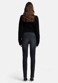 Czarny sweter i dopasowane ciemne jeansy o gładkiej fakturze. Jeansy mają pięć kieszeni, średni stan i zwężane nogawki.
