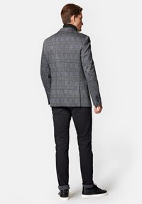 Szary marynarka w kratę z niebieskimi akcentami, dopasowany krój i klapy w szpic. W połączeniu z czarnymi spodniami i teksturowanymi czarnymi sneakersami.