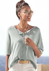 Hellgrünes Hemd mit kurzen Ärmeln, lockerer Passform, strukturiertem Stoff und Kragen, kombiniert mit einem beige Gürtel und Sonnenbrille.