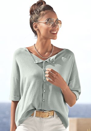 Hellgrünes Hemd mit kurzen Ärmeln, lockerer Passform, strukturiertem Stoff und Kragen, kombiniert mit einem beige Gürtel und Sonnenbrille.