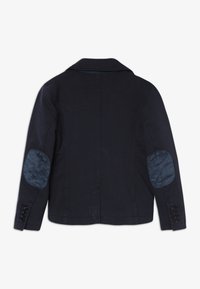Blazer bleu foncé avec des coudières contrastantes et quatre boutons sur chaque poignet, présenté de dos.