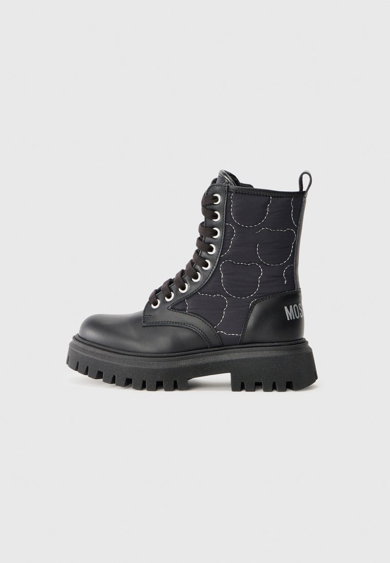 Bota de combate negra con punta de cuero brillante y caña de tejido texturizado que presenta un patrón acolchado. Suela de goma negra y gruesa con detalle de logo.